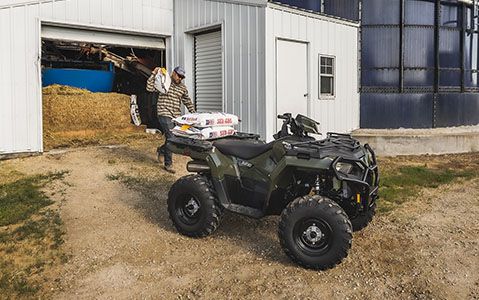 sportsman 450 vehicle parked next to a cow barn with a man in the background