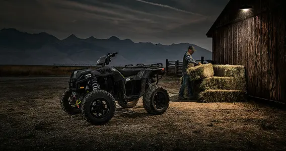 man working with square bales near a sportsman xp 1000 s atv