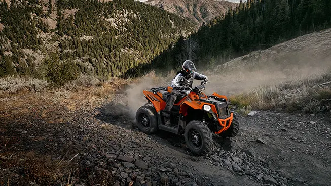 side profile of an orange burst scrambler atv on a hillside