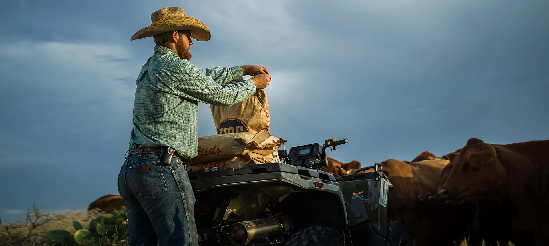 farmer loading feedbags onto the rear end of his sportsman 450 atv