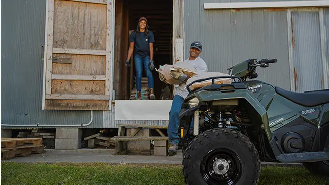 man hauling feedbags and loading them on the front of his sportsman 450 atv