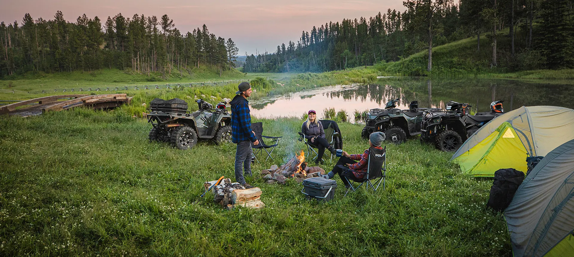 friends sitting around a fire near their sportsman 570 atvs