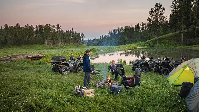 friends sitting around a fire near their sportsman 570 atvs
