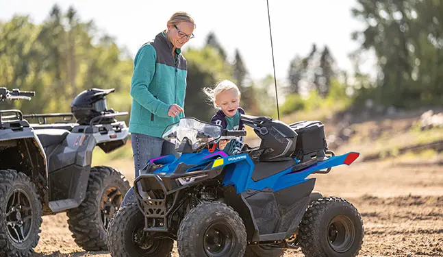 Kid getting onto a 2025 Polaris Outlaw 70 EFI youth ATV.