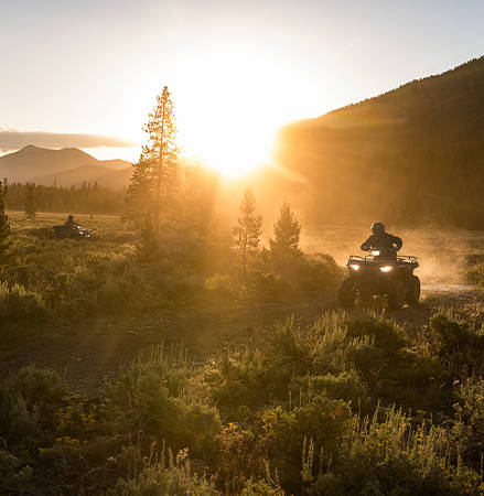 Riders at sunset showcasing the steerable pod headlights on a 2025 Polaris Sportsman 450 ATV.