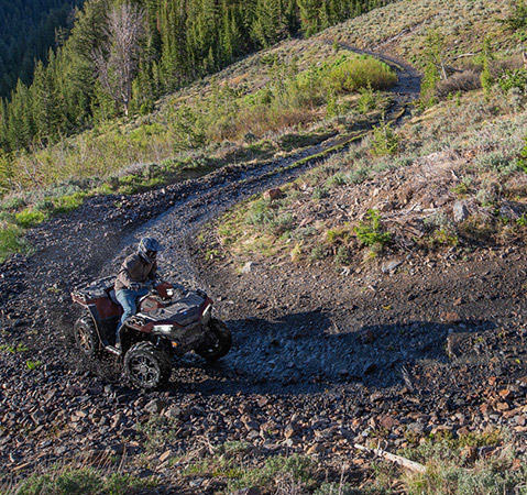 Man on a Polaris Sportsman 850 4-wheeler exploring scenic mountain terrain.