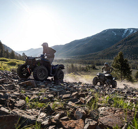 Two Polaris Sportsman 850 ATVs navigating a challenging mountain trail on a group ride.