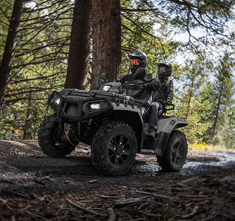 2 people riding through the forest on a 2025 Sportsman Touring XP 1000 Trail ATV.