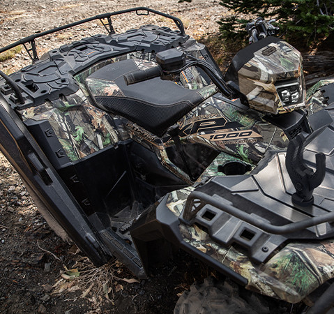 Overhead view of a camouflaged Polaris Sportsman XP 1000 with storage compartments and seating for two, parked in a natural, rocky setting.