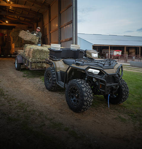 A farmer loading square bales onto a trailer pulled by the strong & versatile 2026 Polaris Sportsman ATV.