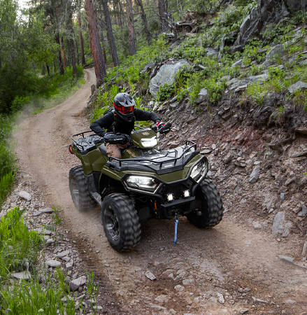 A rider on a 2026 Polaris Sportsman 570 ATV with the LED headlights illuminated.