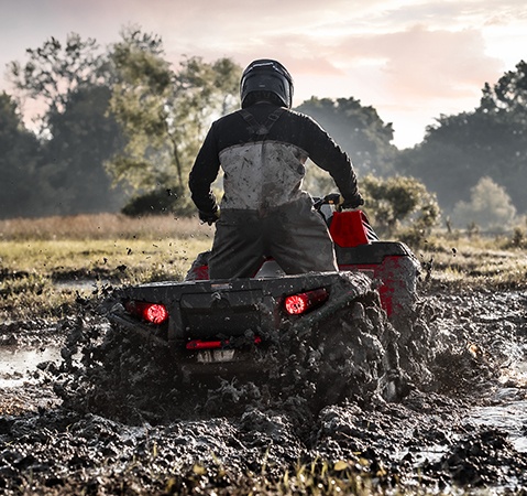 A rider on a 2026 Polaris Sportsman Mud Edition ATV driving through a mud pit and showcasing the independent rear suspension.