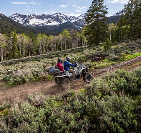 Deux personnes sur un VTT biplace Polaris Sportsman Touring 570 2026 en randonnée tout-terrain avec des montagnes en arrière-plan.
