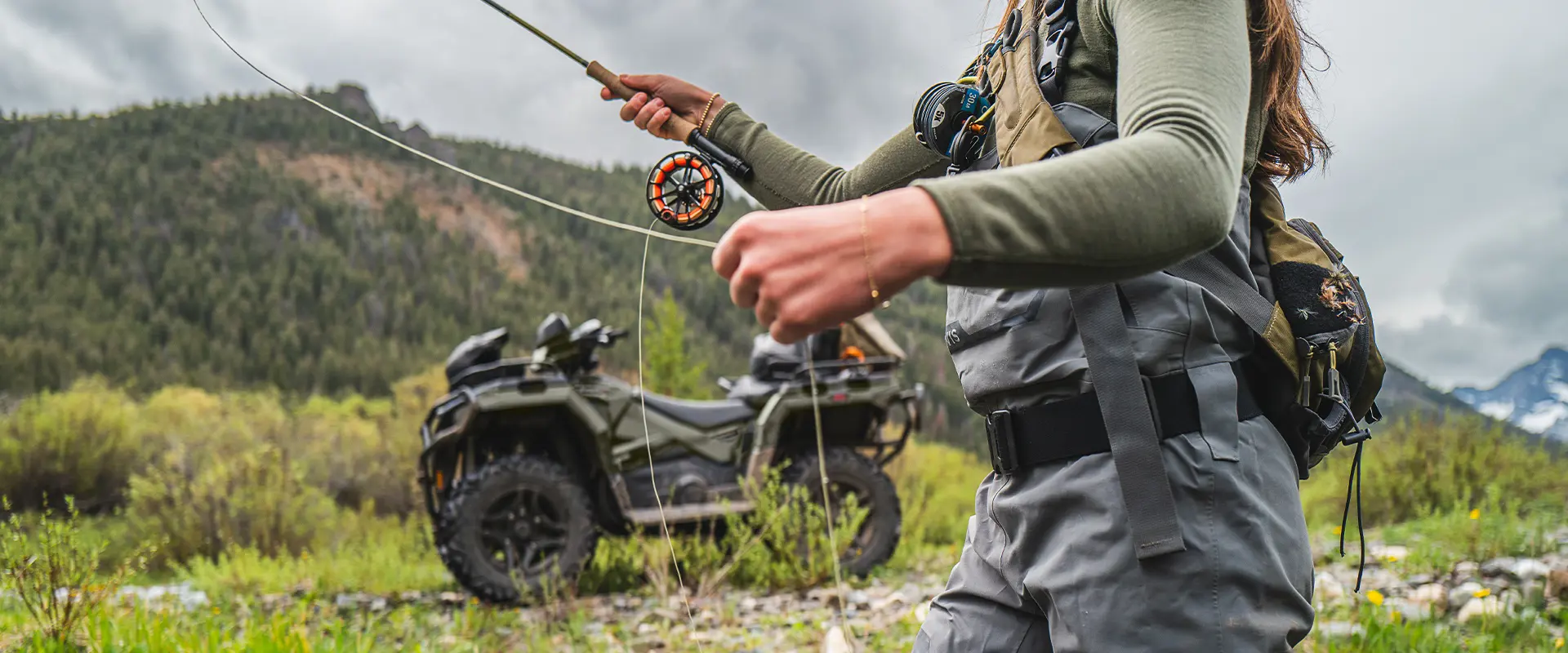A woman fly fishing with her 2026 Polaris Sportsman Touring 570 2-up ATV in the background.