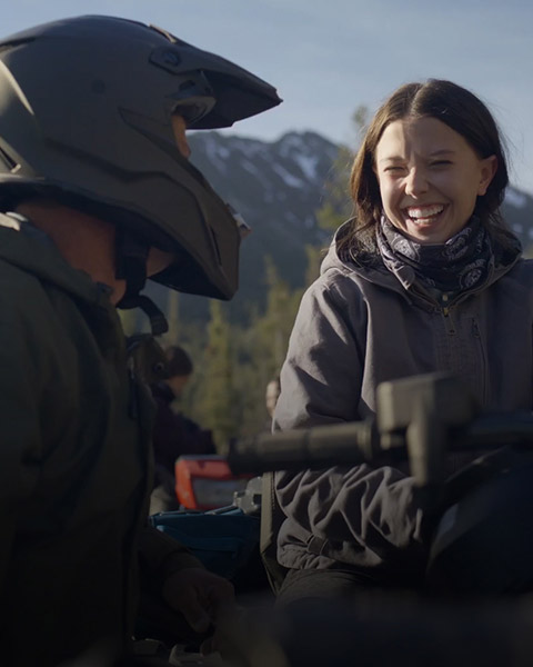 A young woman with a wide smile is enjoying a ride with another person using a helmet on a Polaris Sportsman Touring 570 ATV.