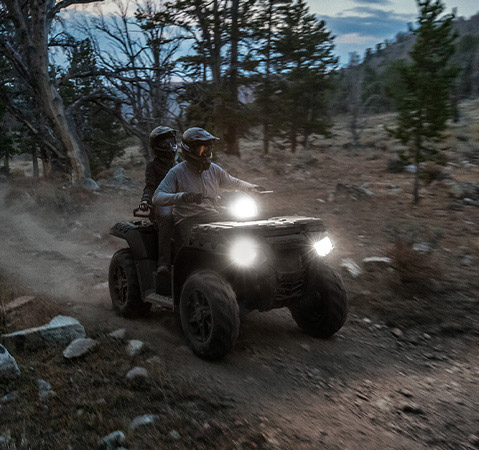 2 riders on a 2026 Polaris Sportsman Touring 850 Premium ATV with the new LED steerable pod and headlights illuminated.