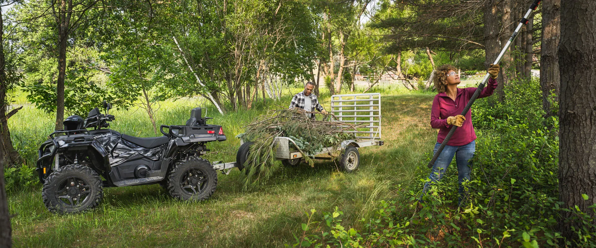 2 people trimming trees and loading limbs onto a trailer pulled by a 2026 Polaris Sportsman X2 570 ATV.