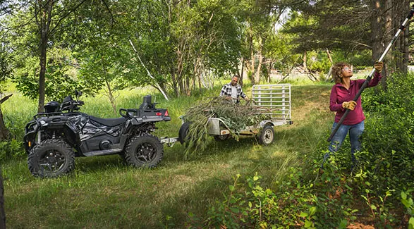 2 people trimming trees and loading limbs onto a trailer pulled by a 2026 Polaris Sportsman X2 570 ATV.