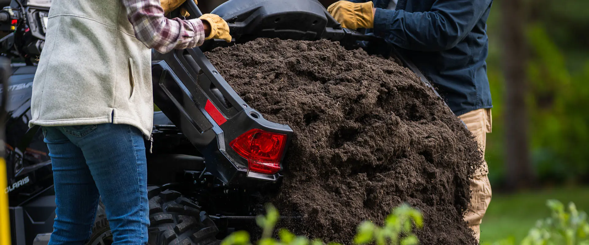 2 people dumping dirt out of the cargo box on a 2026 Polaris Sportsman X2 570 ATV.
