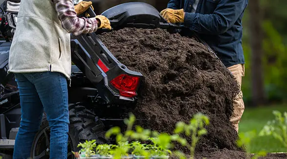 2 people dumping dirt out of the cargo box on a 2026 Polaris Sportsman X2 570 ATV.