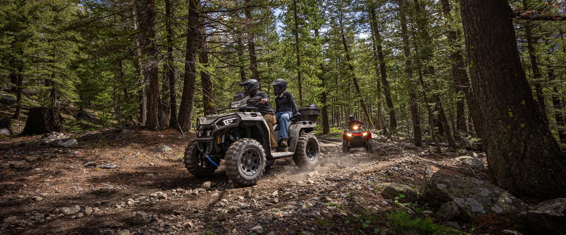 2 groups of people riding 2-up 2026 Polaris Sportsman X2 570 ATVs through the forest.