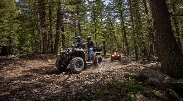2 groups of people riding 2-up 2026 Polaris Sportsman X2 570 ATVs through the forest.