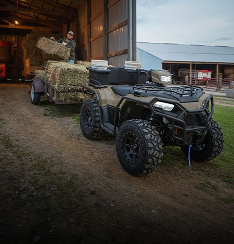 A farmer loading square bales onto a trailer pulled by a 2027 Polaris Sportsman ATV.