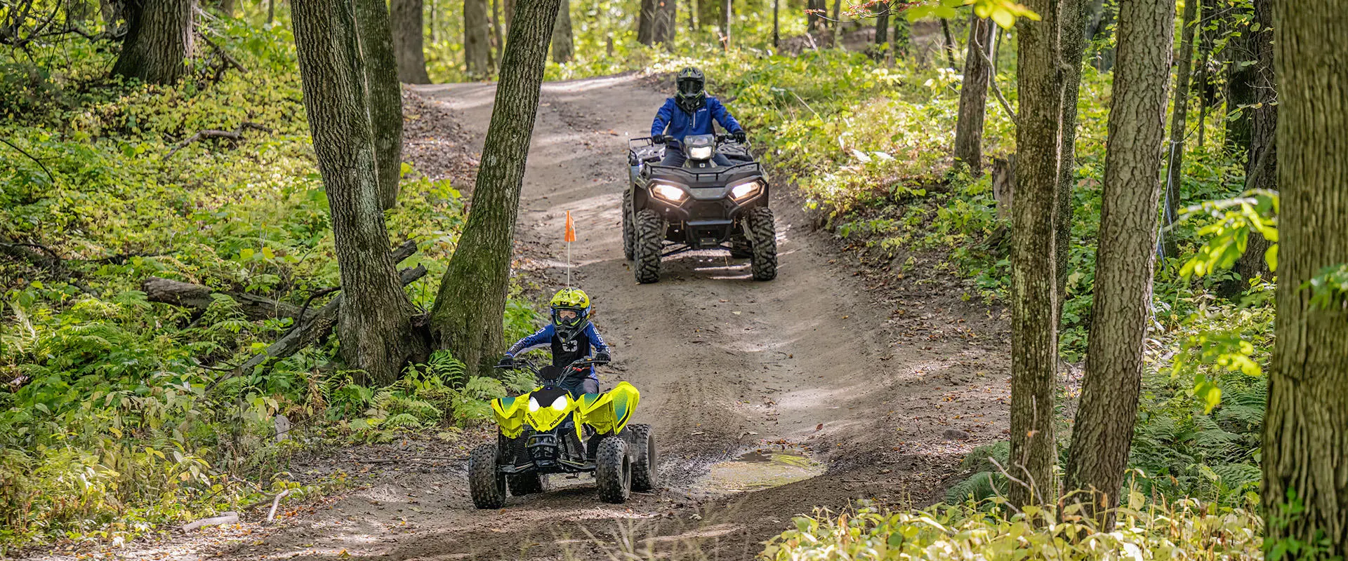 A kid on a Lime Squeeze 2027 Polaris Outlaw 110 EFI youth ATV on a trail.