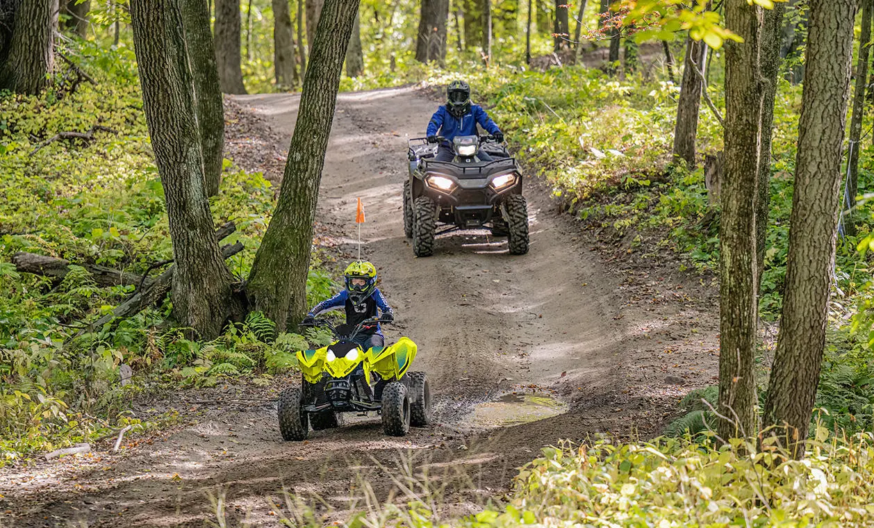 A kid on a Lime Squeeze 2027 Polaris Outlaw 110 EFI youth ATV on a trail.
