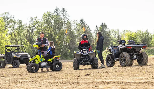2 kids on their Polaris youth ATVs getting ready for a ride.