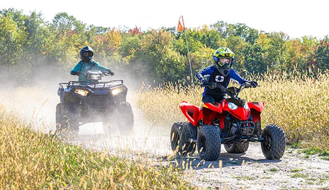 A kid trail riding on an Indy Red 2027 Polaris Outlaw 110 EFI youth ATV.