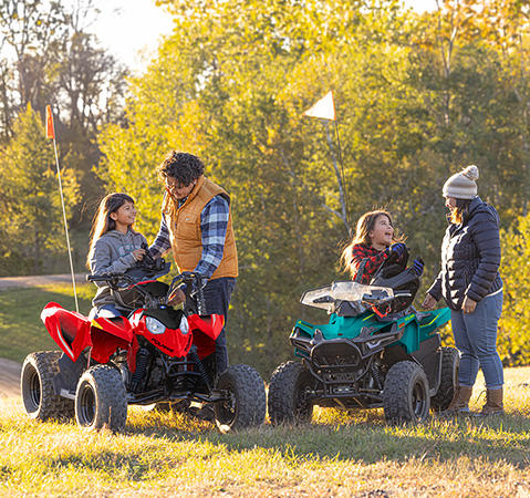 2 parents helping their kids on their 2 Polaris youth ATVs.