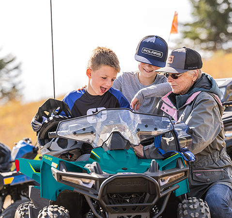 2 kids and a grandparent looking at accessories on their 2026 Polaris Outlaw 70 EFI youth ATV.