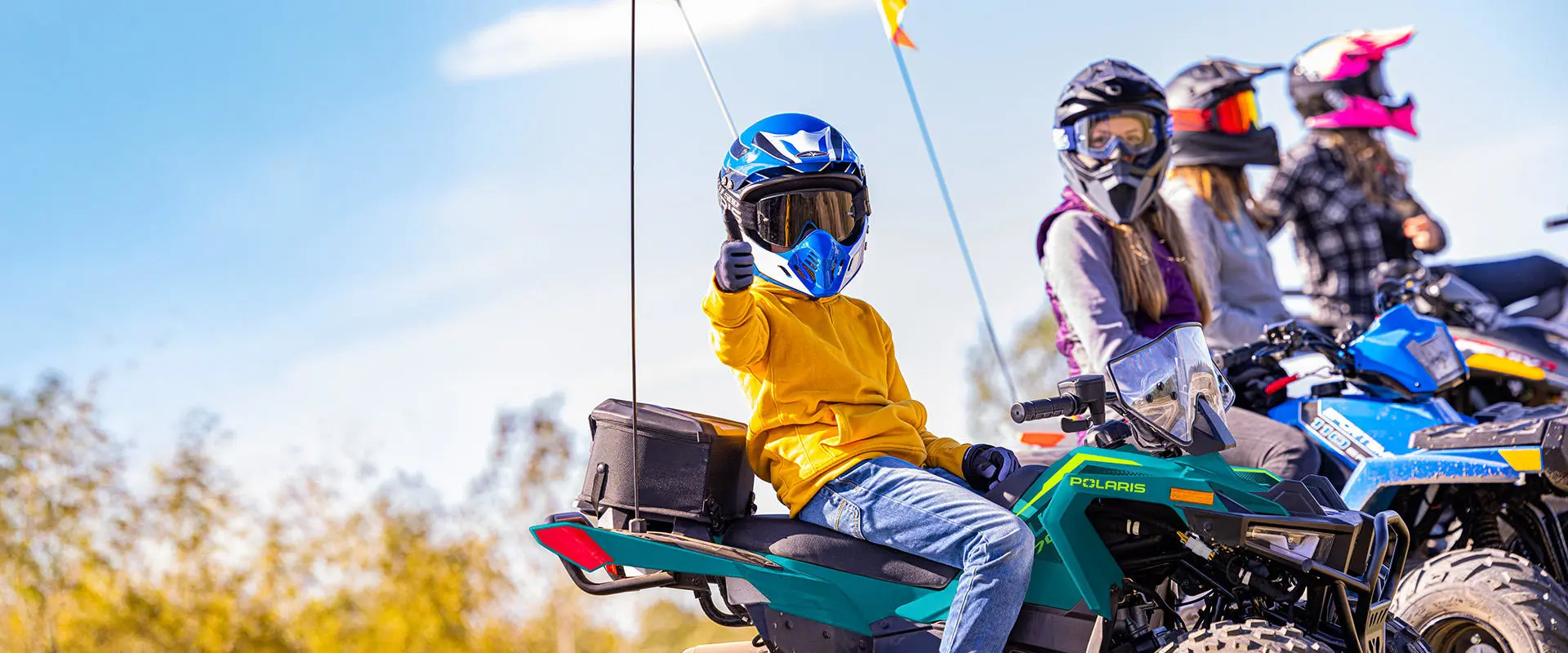 A kid giving a thumbs up while sitting on a 2026 Polaris Outlaw 70 EFI youth ATV.