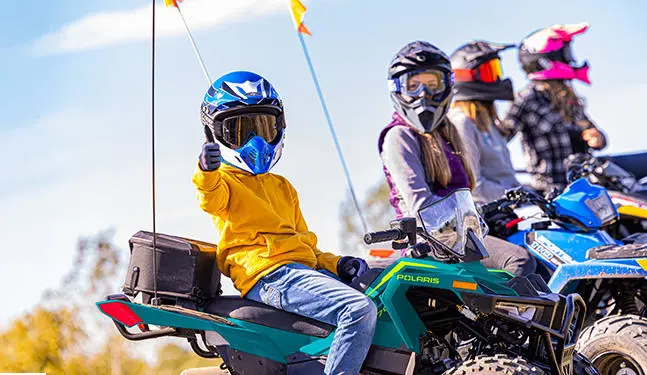A kid giving a thumbs up while sitting on a 2026 Polaris Outlaw 70 EFI youth ATV.