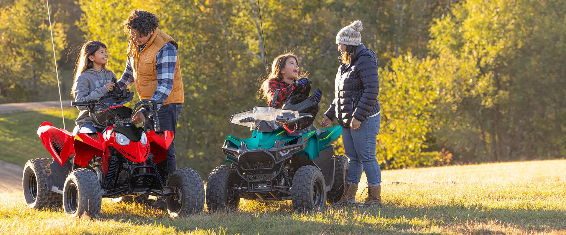 2 kids chatting with their parents while sitting on their Polaris youth ATVs.