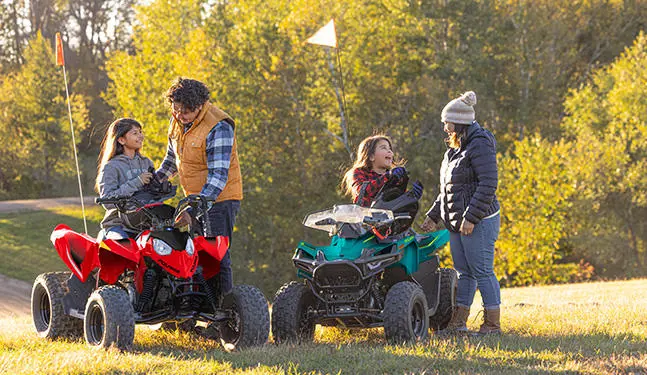 2 kids chatting with their parents while sitting on their Polaris youth ATVs.