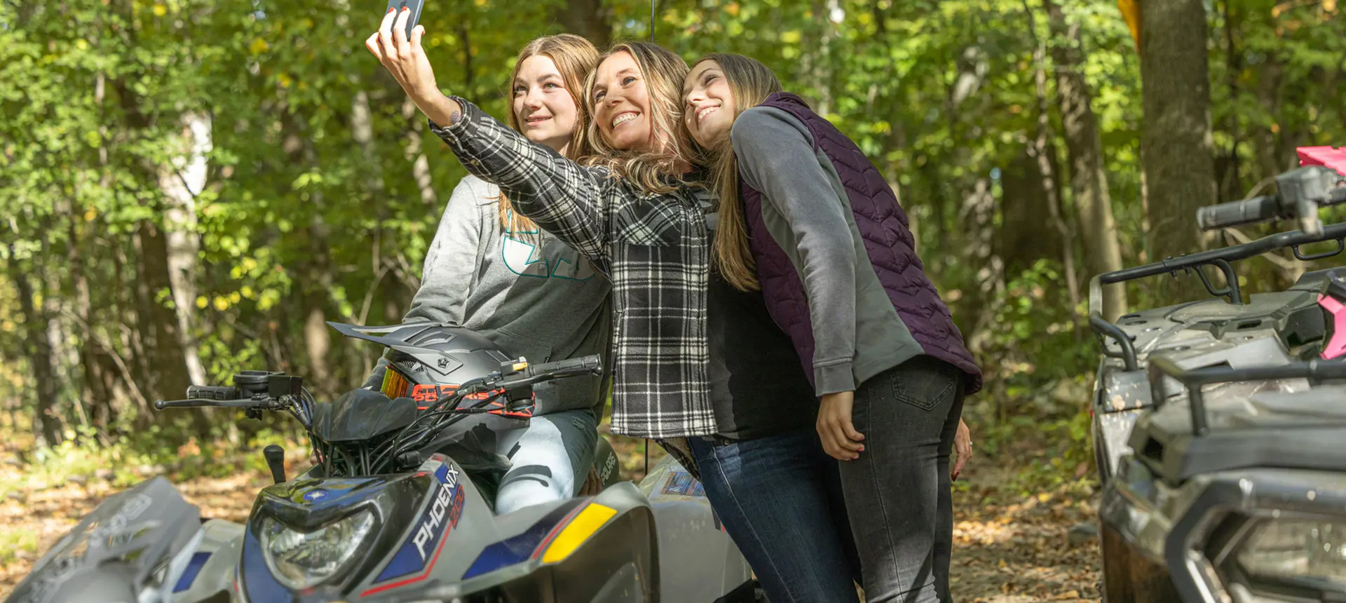 3 girls taking a selfie near a 2027 Polaris Phoenix 200 youth ATV.