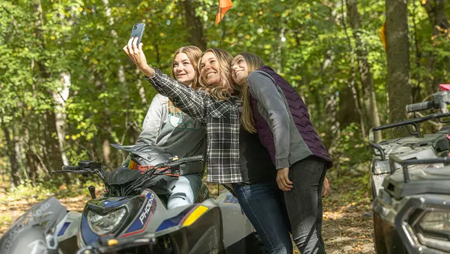 3 girls taking a selfie near a 2027 Polaris Phoenix 200 youth ATV.