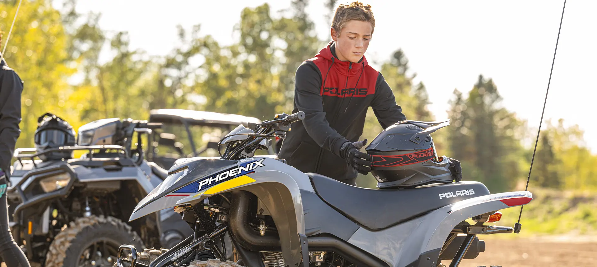 A boy grabbing his helmet to ride his 2027 Polaris Phoenix 200 youth ATV.