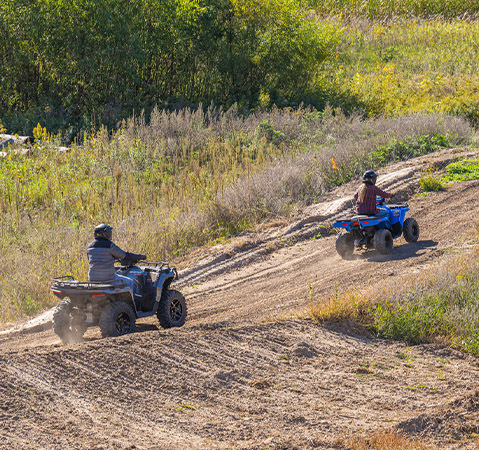 A kid on a 2027 Polaris Sportsman 110 EFI youth ATV riding behind another rider on a Polaris youth ATV.