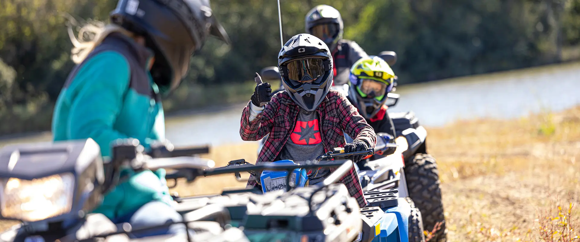 A kid giving a thumbs up from a 2027 Polaris Sportsman 110 EFI youth ATV to other youth ATV riders.
