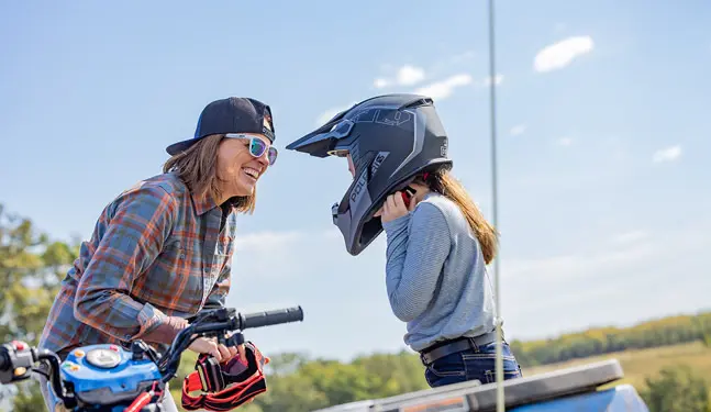 A mom talking to her kid on a 2027 Polaris Sportsman 110 EFI youth ATV.