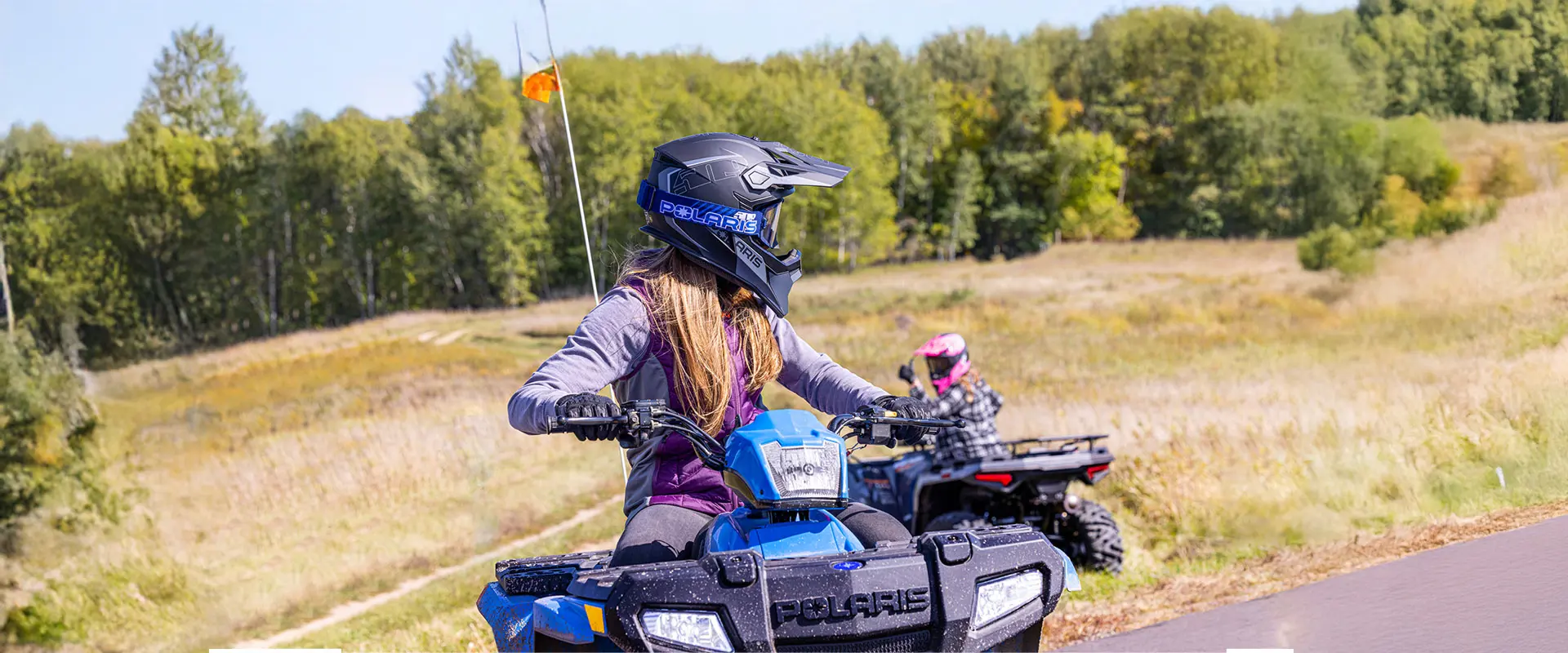 A rider on a 2027 Polaris Sportsman 110 EFI youth ATV looking back at another rider on a Polaris youth ATV.