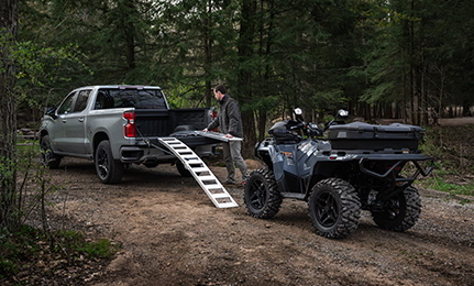 A man grabbing ramps from his truck bed to load up his 2027 Polaris Sportsman 500 ATV.