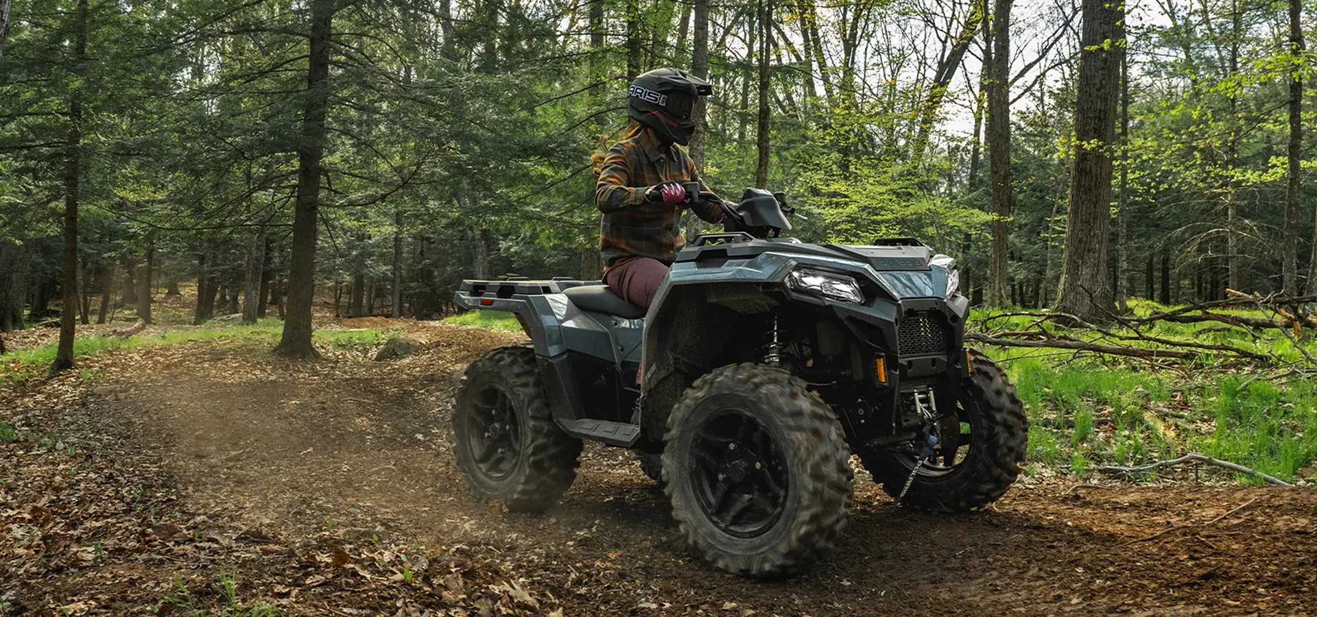 A woman riding a 2027 Polaris Sportsman 500 ATV on a forest trail.