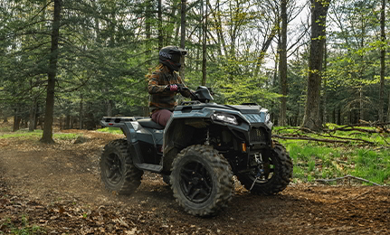 A woman riding a 2027 Polaris Sportsman 500 ATV on a forest trail.