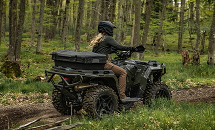 Rear view of a woman on a 2027 Polaris Sportsman 500 ATV cruising down a forest trail.