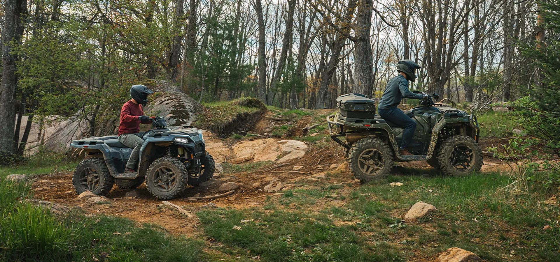 2 people riding 2027 Polaris Sportsman 500 ATVs on a trail in the forest.