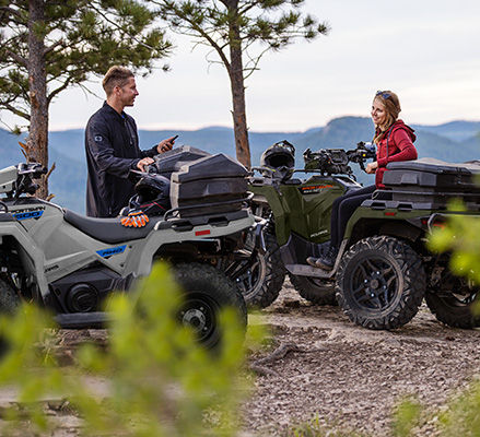 2 people relaxing after a ride on their 2027 Polaris Sportsman 600 four-wheelers.